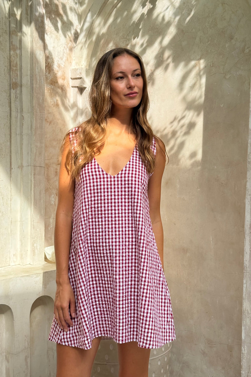 Woman wearing a red and white checkered dress standing against a textured wall.